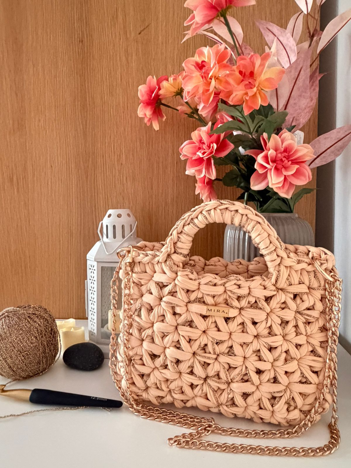 Woven handbag with chain detail on a surface with flowers and lantern in the background